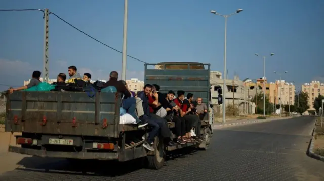 Dozens of Palestinian people sitting on the back of an empty lorry bed, fleeing their homes in northern Gaza