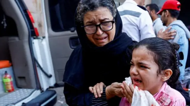 A Palestinian girl in tears holds a blood-stained tissue to her face as she is led away by a woman