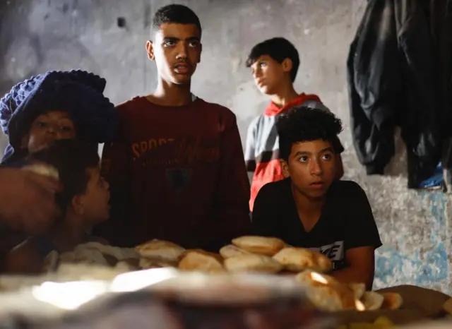 Palestinian children wait for bread baked on firewood amid fuel and electricity shortages in Gaza