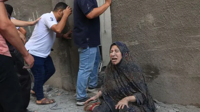 A woman looking anguished sitting on the floor, other people around peering in a doorway