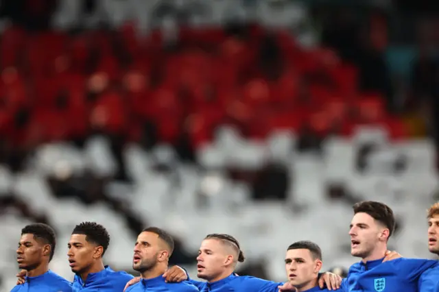 England players sing the anthem as fans hold placards to make a flag behind.