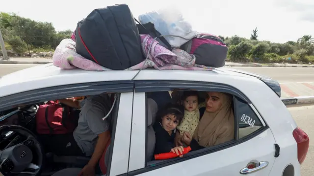 A Palestinian woman and her family sit in a car, with their belongings strapped to the top, as they prepare to move to another region