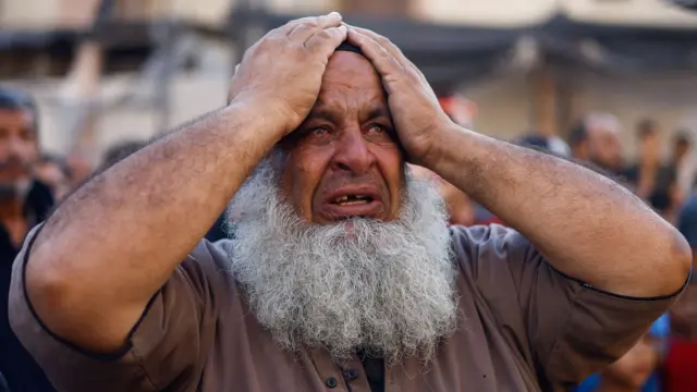 Headshot of a man crying and holding his hands to his head as he looks on