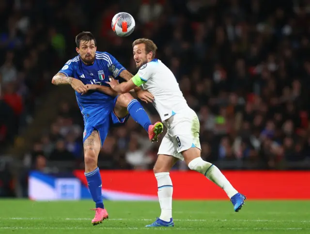 Kane and Acerbi battle for the ball in an aerial duel.