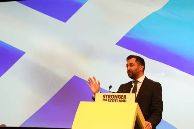 Yousaf stands in front of saltire at a podium