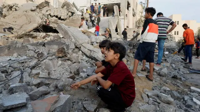 A boy sits among rubble and looks anguished