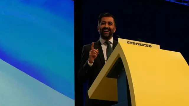 Humza Yousaf stands at a podium with the saltire in the background