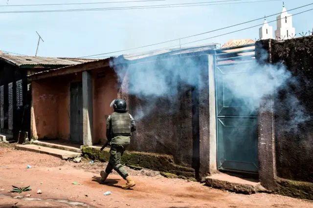 A Police officer fires tear gas as mass protests broke out the morning after preliminary results were released for five communes in Conakry on October 21, 2020