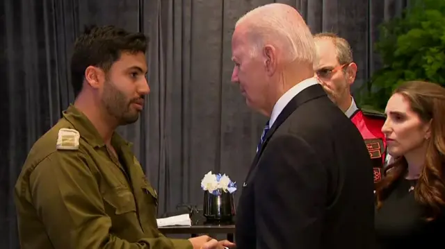 President Biden speaks to a man wearing a green uniform