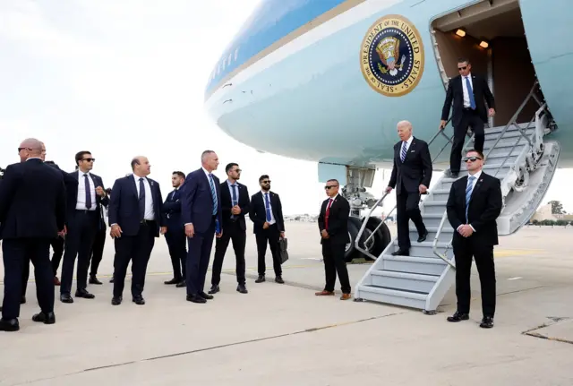 Biden walks down the steps of Air Force One surrounded by lots of security