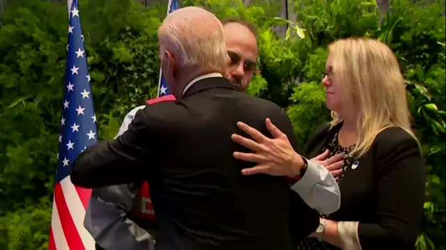 President Biden hugs a man wearing a read tabbard