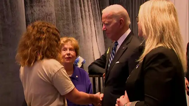 President Biden shakes hands with a woman while she speaks to him