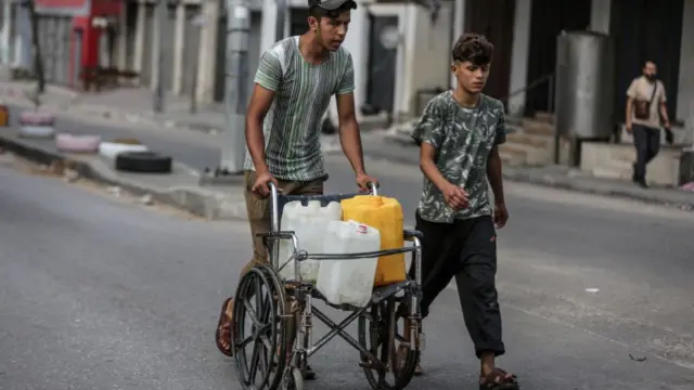 Palestinians carry containers of water in a wheelchair