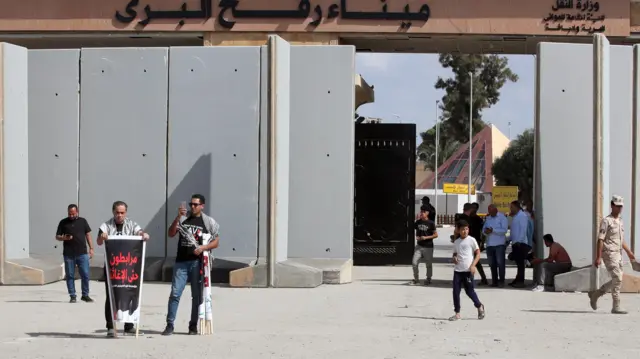 A volunteer from a humanitarian aid organisation holds placard reading in Arabic "stationed until relief delivered" during a protest outside border gate between Egypt and Gaza