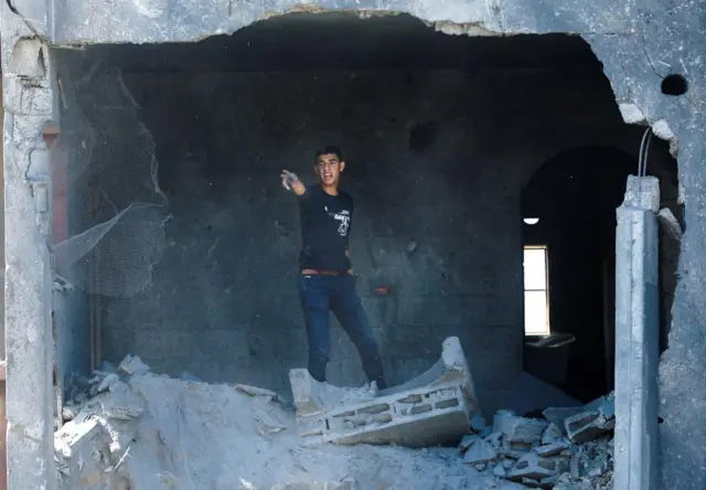 A man gestures at the site of an Israeli air strike, he is point out of a large hole in a building