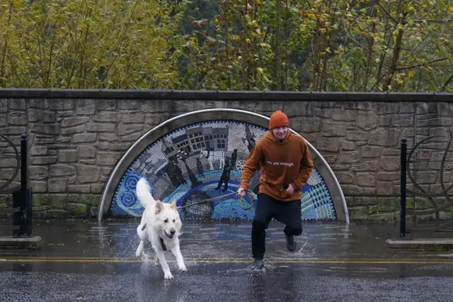 A man and his dog jumping into a puddle on the street