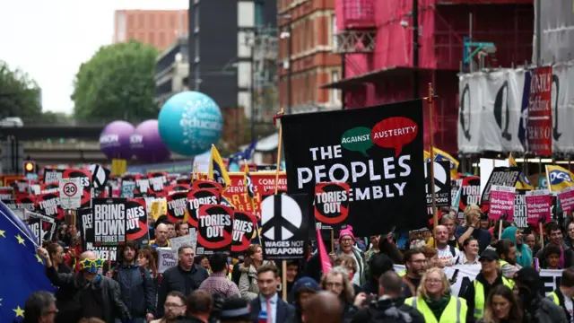 Thousands of protesters walk through the streets of Manchester, some holding signs that read 'Tories out' on 1 October