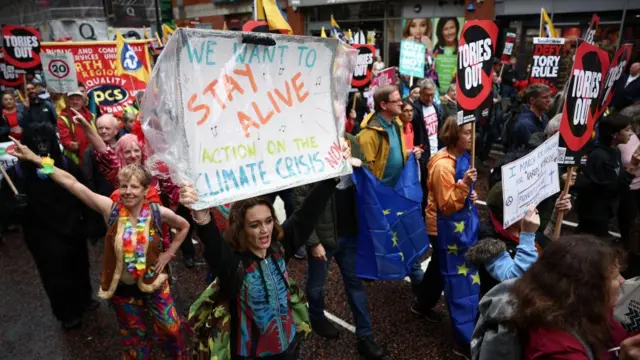 A woman holds a sign that reads 'We want to stay alive, action on the climate crisis' at a protest in Manchester 1 October 2023