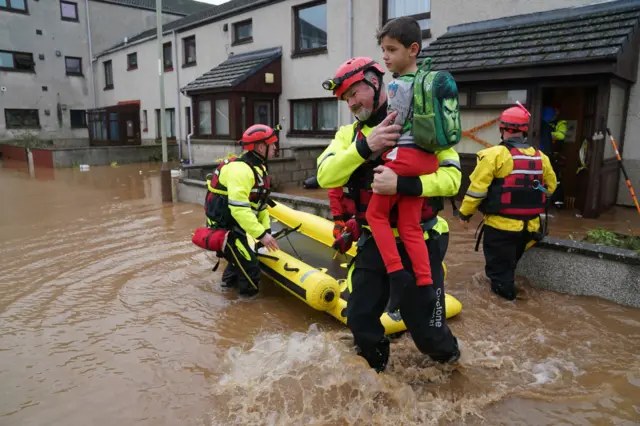 A member of the emergency services carries a boy from a house in Brechin, Scotland, as Storm Babet batters the country