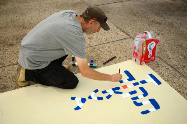 A man paints a message reading "Hope" in Hebrew