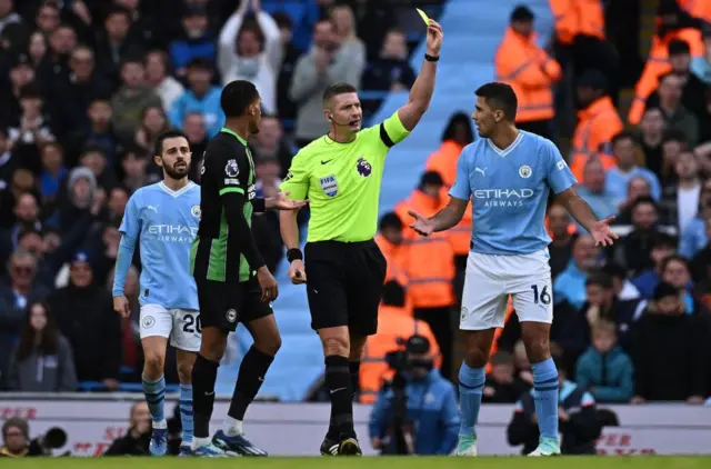 Referee Tim Robinson shows a yellow card to Manchester City's Spanish midfielder Rodri