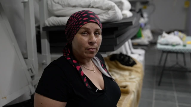 A women (with no hair but her head covered with a scarf) looks directly at the camera