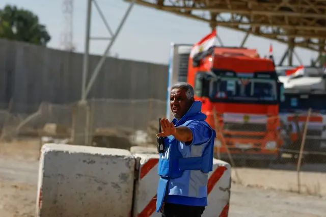 A man in a UN vest gestures in front of trucks at the crossing