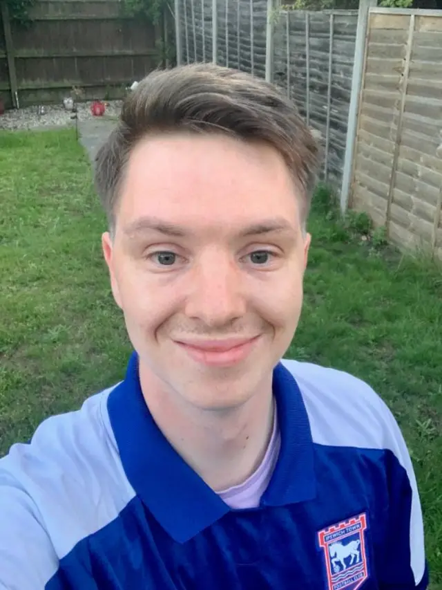 Luke Penning standing in his back garden. He is wearing a blue Ipswich Town football shirt and has short brown hair.