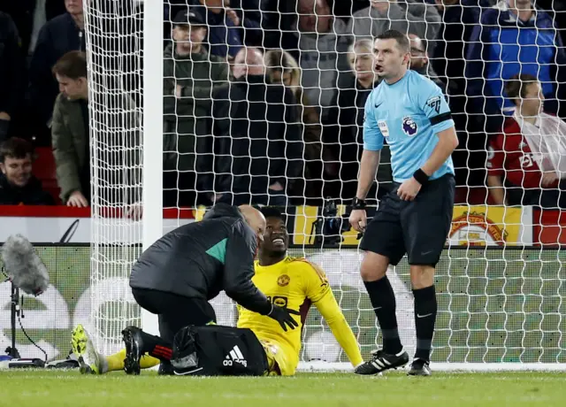 Onana is tended to by a physio as the referee watches on.