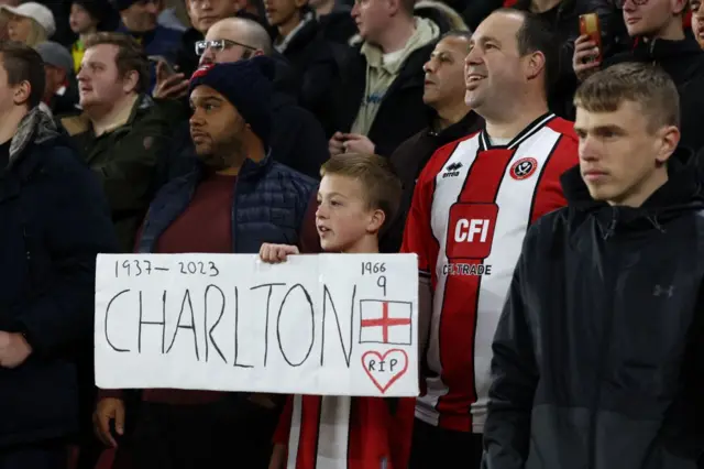 A young fan holds a sign in tribute to the late Sir Bobby Charlton.