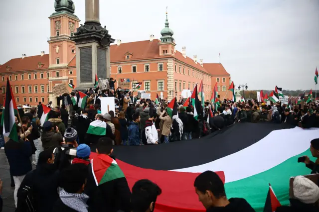 A crowd of protesters holding a large Palestinian flag in Warsaw