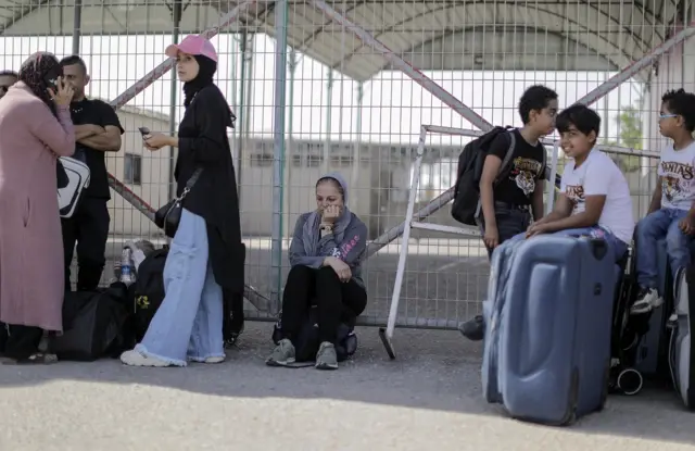 People wait at the Rafah crossing with suitcases