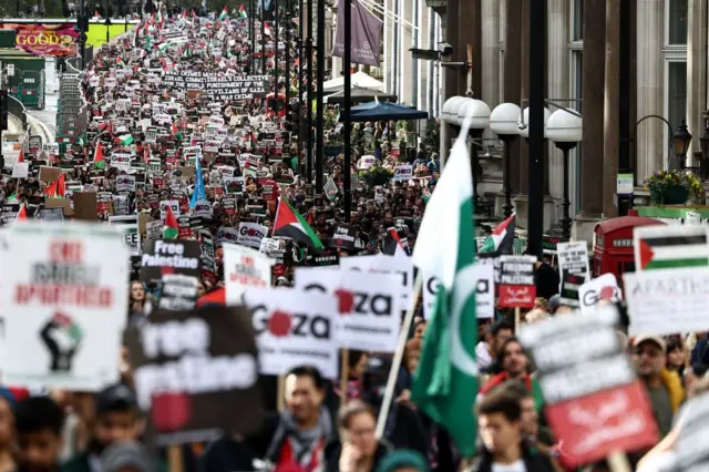 A huge crowd of people with placards and Palestinian flags march down a London street