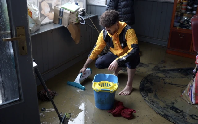 Ahmet is crouched down in the floodwater in his bare feet trying to suction off some of the flood water.