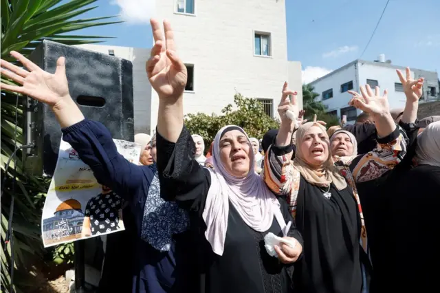 Women look distressed and hold their hands in the air during a funeral in the West Bank