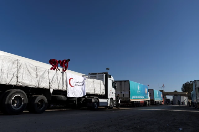 Aid workers stand on top of trucks with are lined up in a queue at the Gaza border