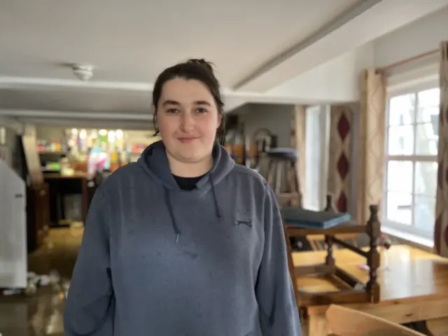 Laura Robinson standing in the pub where piles of furniture can be seen in the background