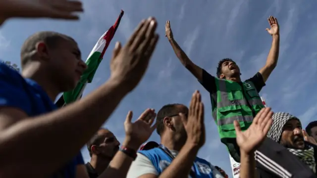 A man sits atop the shoulders of another, with his hands thrown up in celebration