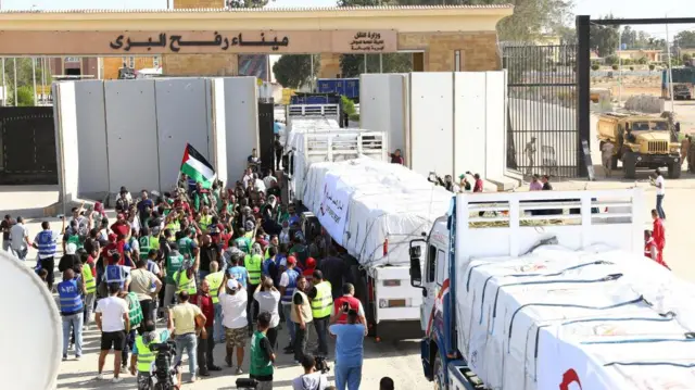 A crowd gathers at the border gate, a Palestinian flag is waved