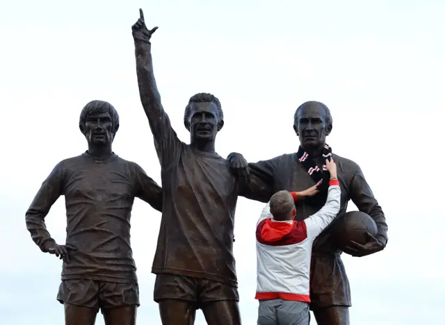 A fan hangs a scarf around the neck of the Sir Bobby Charlton statue outside Old Trafford.