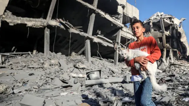 A child carries a cat among destroyed buildings and roads after Israeli airstrikes in Al-Zahra region of Gaza