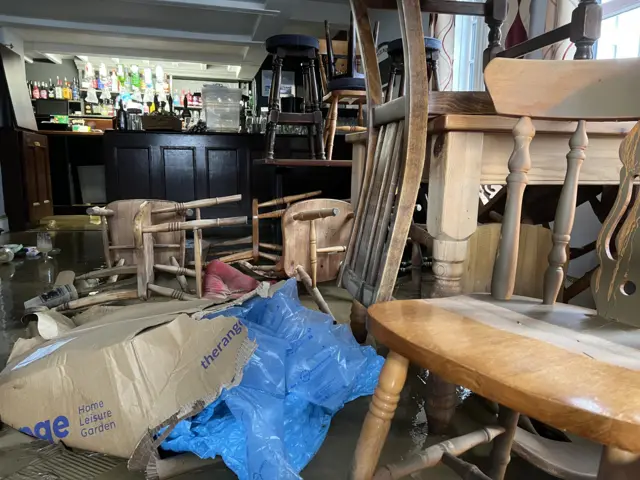 Piled up and overturned furniture amid standing water in the pub.