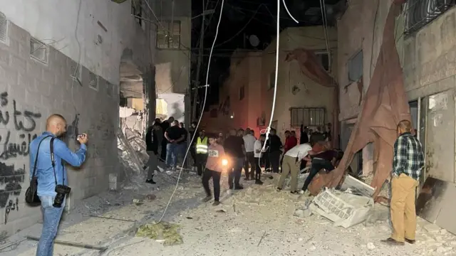 People stand near a building damaged in an Israeli air strike