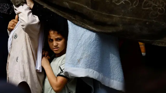 A child looks on as Palestinians queue to buy bread from a bakery