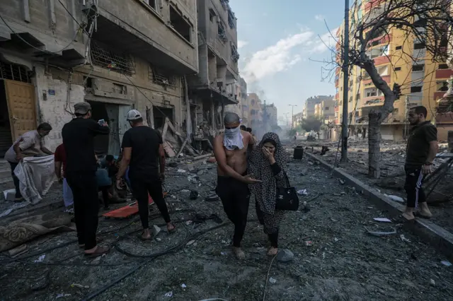 A man helps a woman (R) flee the area as others (L) attend to a victim following an airstrike in Gaza