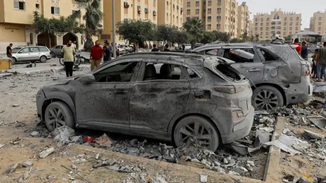 A burnt-out car parked among debris