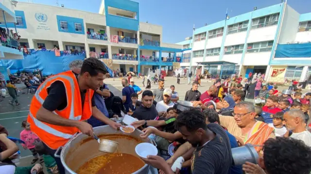 Volunteers hand out food to Palestinians living in a UN-run school