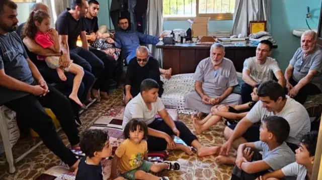 Members of the household gather together in a room and sit on the floor