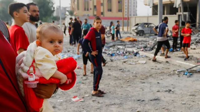 A person holds a child as Palestinians gather at the site of Israeli strikes on a house in Khan Younis in the southern Gaza Strip, October 23, 2023.