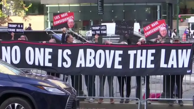 A small group of people stand in front of a silver barrier holding a big banner saying 'no one is above the law'